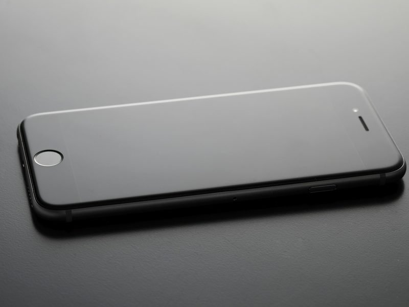 A black iPhone with a glass screen lying on a dark table