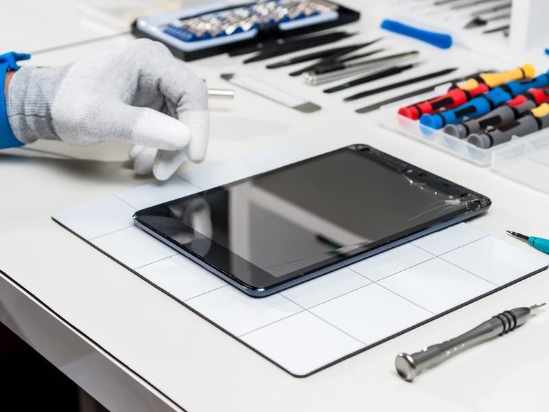 A tablet on a repair mat surrounded by precision repair tools